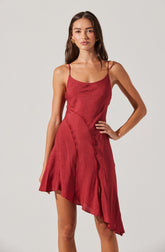 A young woman is wearing a sleeveless, red dress with spaghetti straps. The dress features an asymmetrical hemline and appears to be made of a shiny, textured fabric.